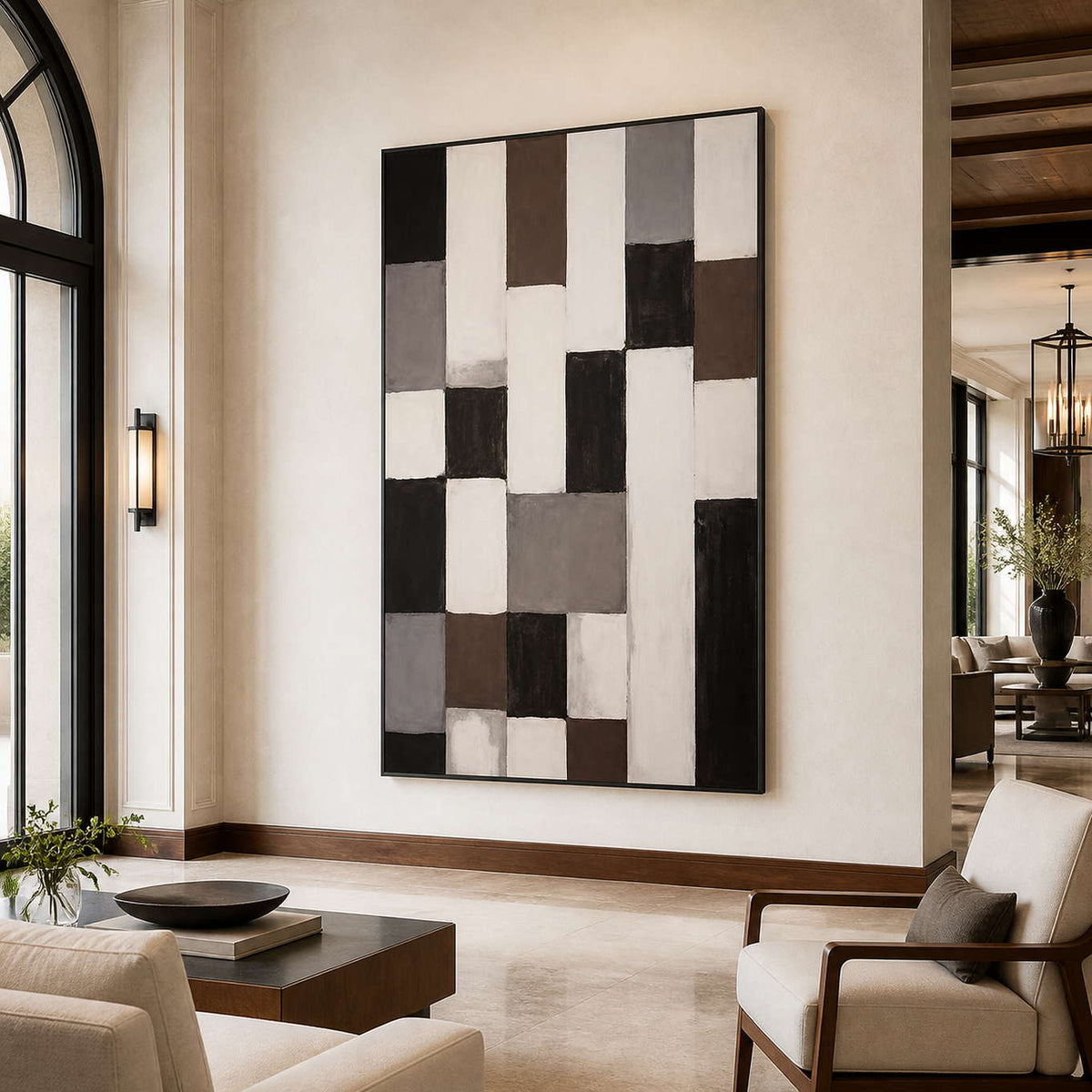 Black framed neutral geometric artwork beside cream lounge chairs in a light hotel lobby.