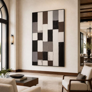 Black framed neutral geometric artwork beside cream lounge chairs in a light hotel lobby.