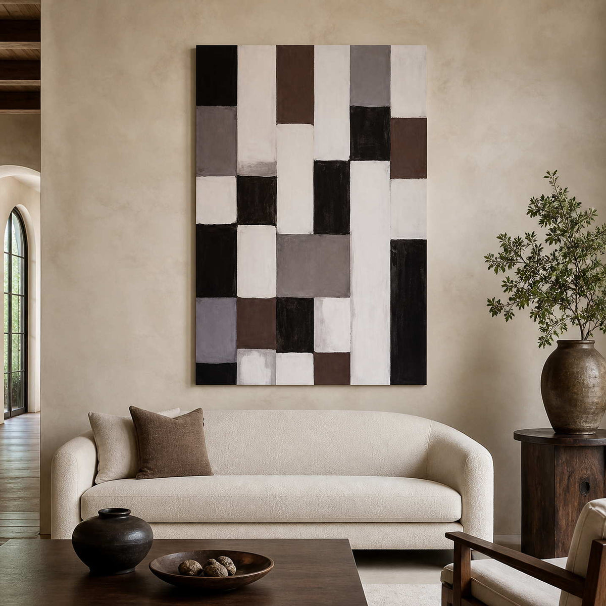 Frameless geometric abstract artwork with neutral rectangles above a curved cream sofa beside leafy branches.