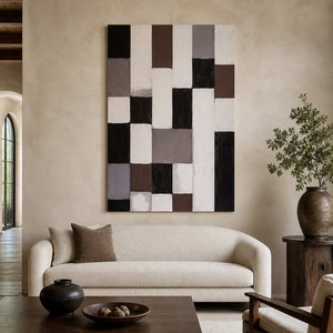 Frameless geometric abstract artwork with neutral rectangles above a curved cream sofa beside leafy branches.
