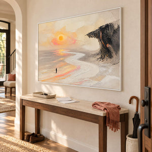 Landscape painting with a lone figure, amber sun, pale shore, and dark cliff in a white frame in an entryway.