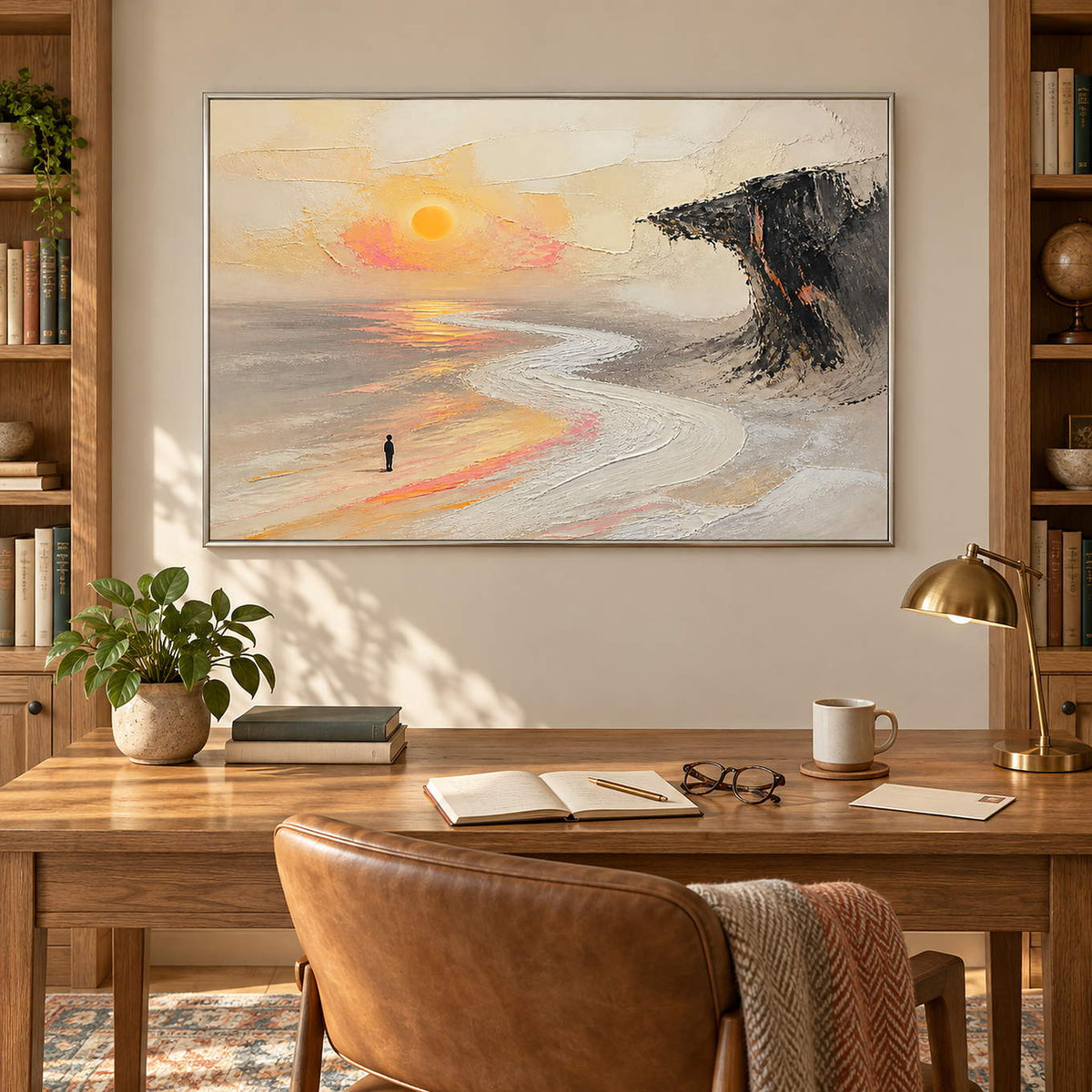 Landscape painting with a lone figure, amber sun, pale shore, and dark cliff in a silver frame in a home office.