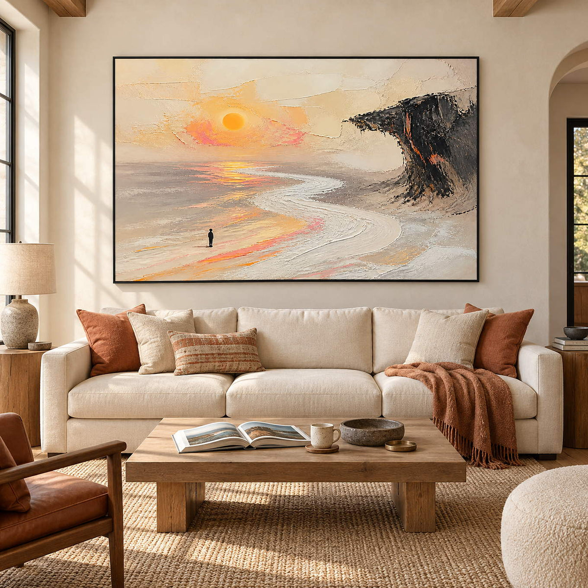 Landscape painting with a lone figure, amber sun, pale shore, and dark cliff in a black frame in a living room.