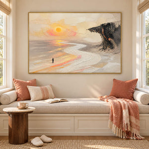 Landscape painting with a lone figure, amber sun, pale shore, and dark cliff in a gold frame in a sunlit seating area.