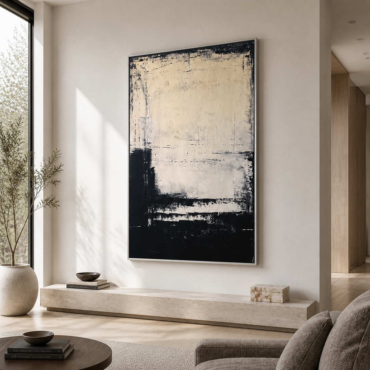 Silver framed cream and dark abstract painting beside a sofa in a bright living room.