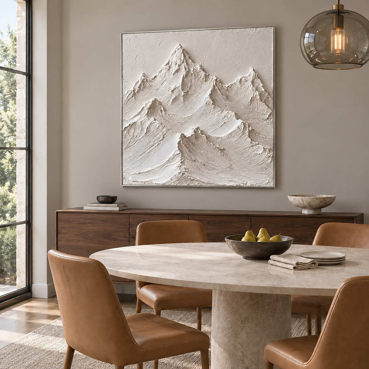 The Mountains Stand Watch in a silver frame above a wood sideboard beside a round stone table and tan chairs.