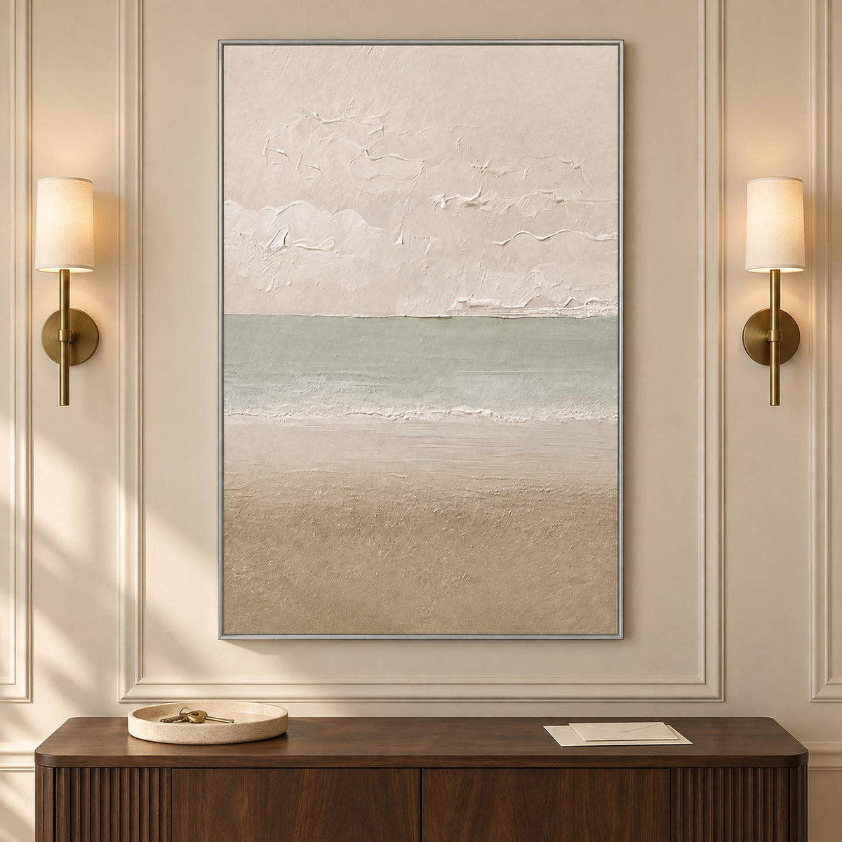 Hand-painted coastal canvas in warm ivory, sea-glass green, and sand, displayed in an entrance hall in a silver frame.