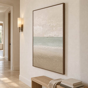 Hand-painted coastal canvas in warm ivory, sea-glass green, and sand, displayed in a hallway in a brown wood frame.