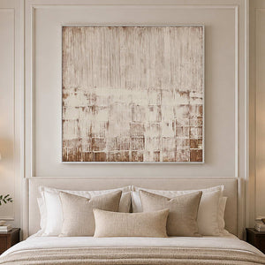 White framed cream and brown abstract artwork above a bed with textured neutral pillows.