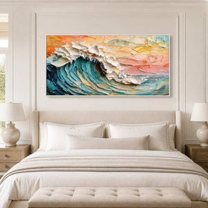 White framed coastal wave painting above a cream upholstered bed between matching lamps.