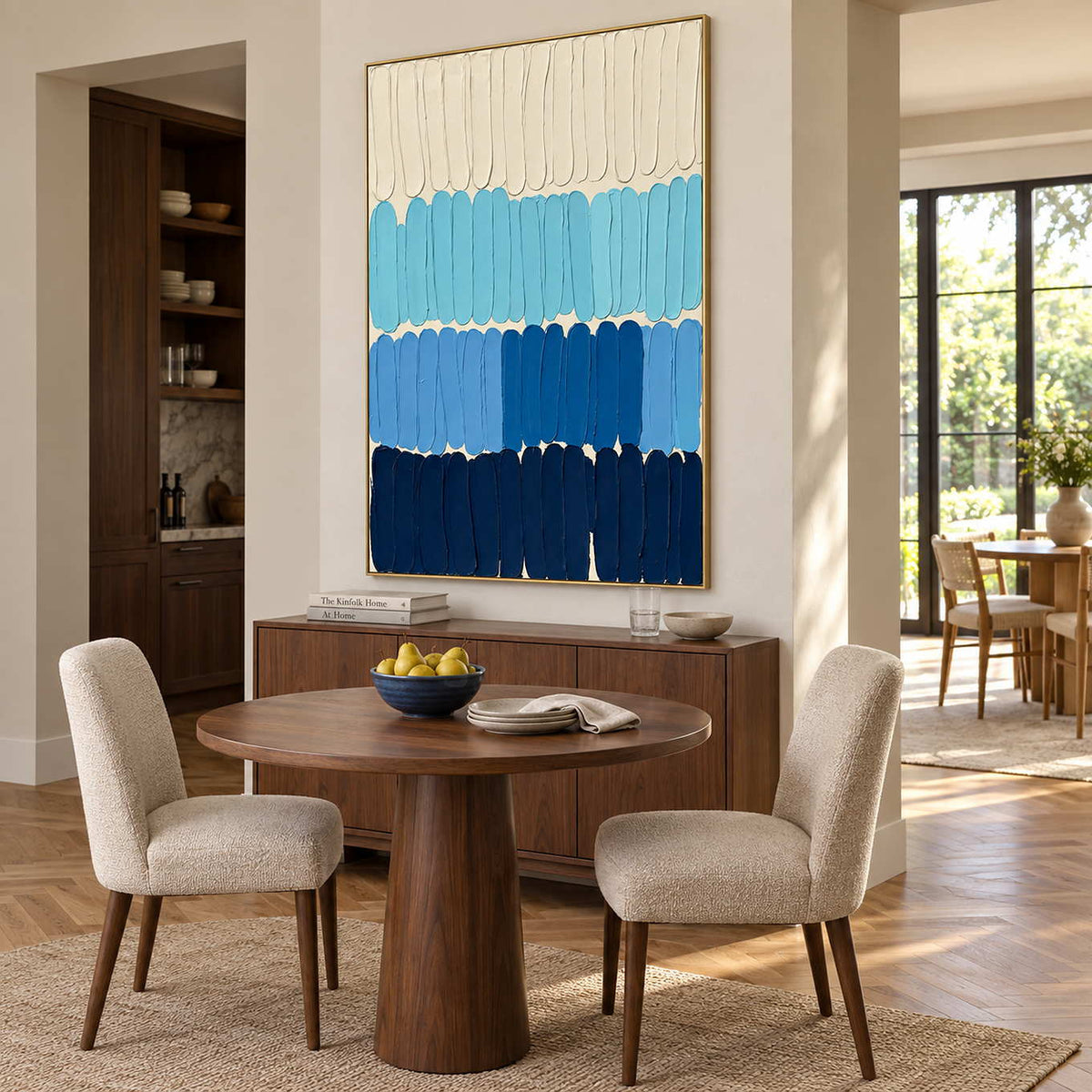The Sea's Rhythm in a gold frame above a sideboard behind a round wood dining table.