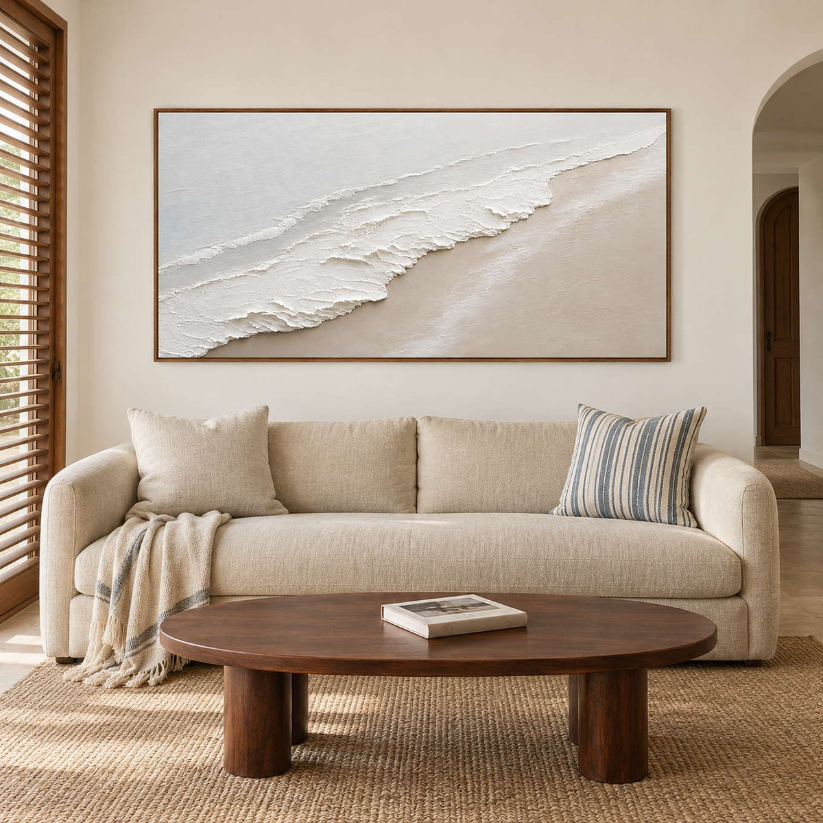 Soft white surf along a pale sandy shoreline in a brown wood frame, displayed above a sofa in a living room.