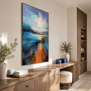 Wood framed blue landscape above bathroom cabinetry with folded towels and a padded stool.