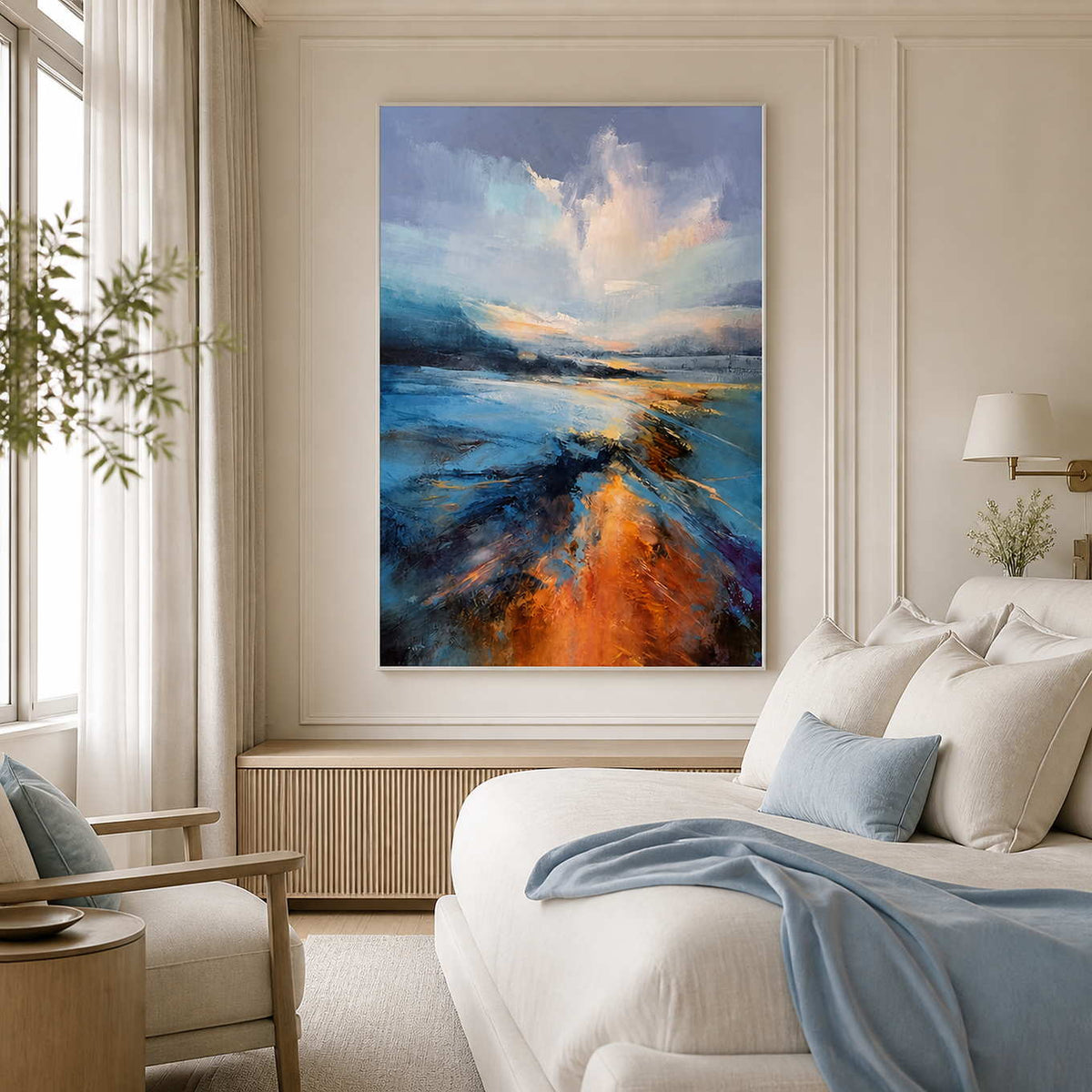 White framed blue landscape beside a cream bed with blue cushions and a blanket.