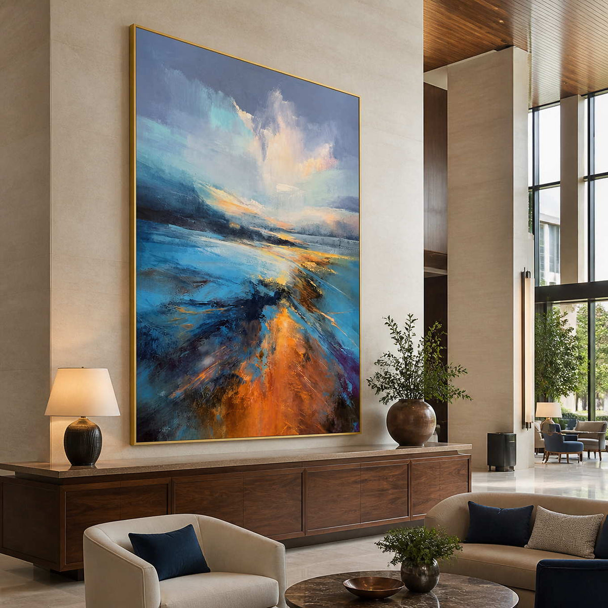 Gold framed shoreline painting above a wooden hotel lobby console beside tall windows.
