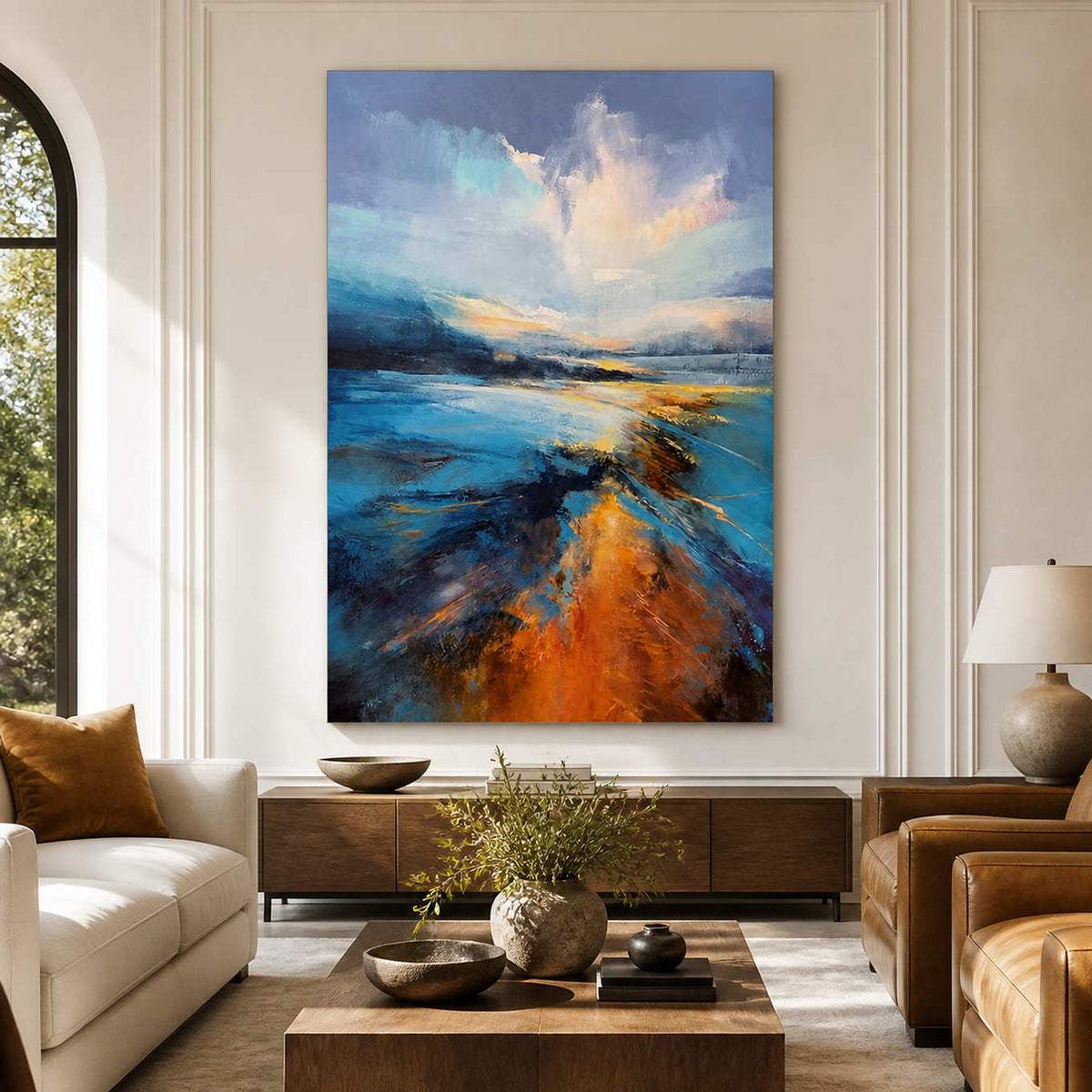 Frameless blue shoreline artwork between cream and tan seating in a sunlit living room.