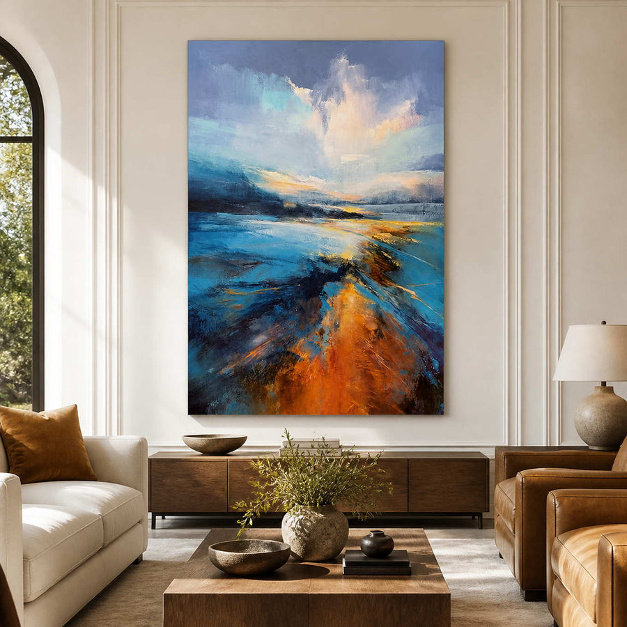 Frameless blue shoreline artwork between cream and tan seating in a sunlit living room.