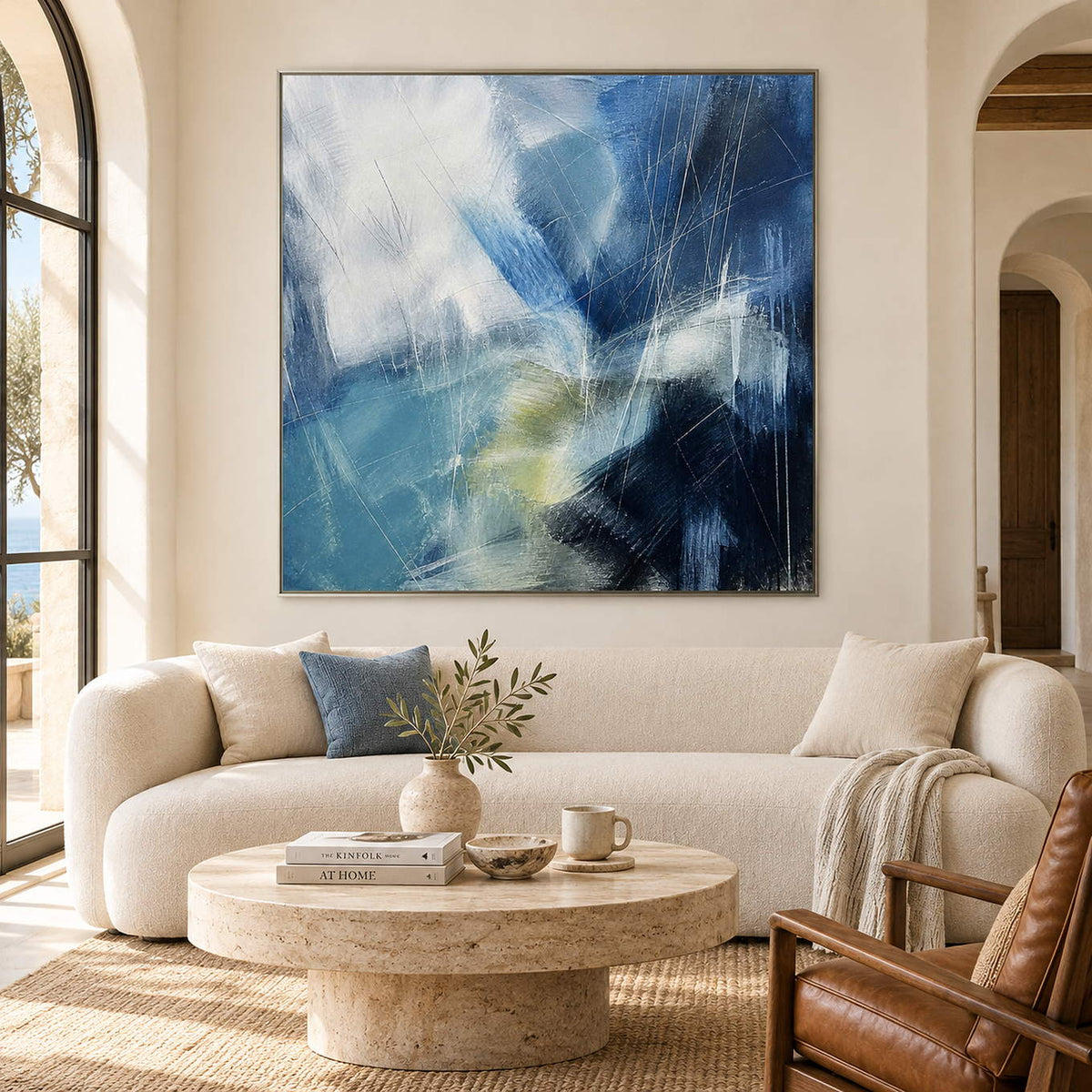 Hand-painted blue abstract canvas with white sweeps and charcoal contrast, displayed in a living room in a silver frame.