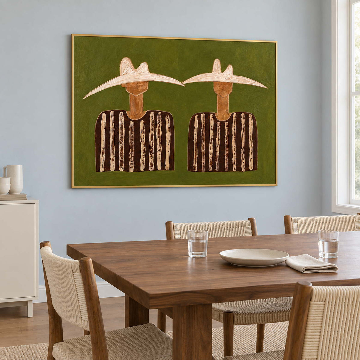 Olive-ground portrait beside a wooden dining table and woven chairs.