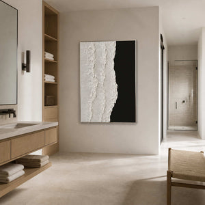 Silver framed textured painting beside an oak bathroom vanity and open towel shelves.