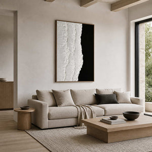 Wood framed textured artwork above a cream sofa in a bright neutral living room.