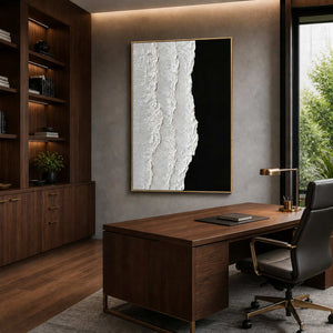 Gold framed black and white artwork above a walnut desk with a black office chair.