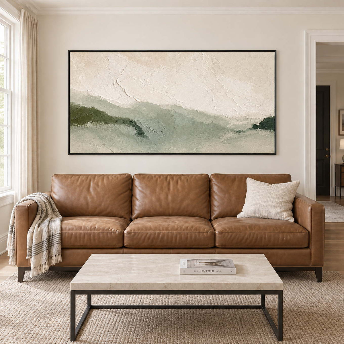 Soft green valley ridges fading beneath a pale textured sky in a black frame, displayed above a sofa in a living room.