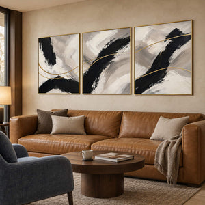 Three vertical abstract panels with black gestures, ivory fields, and gold lines, displayed in a lounge with gold frames.
