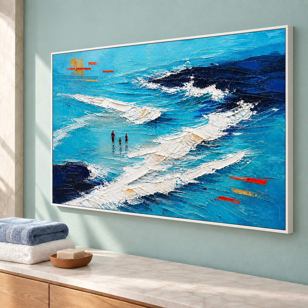 Turquoise coastal painting with three figures among white breaking waves in a white frame beside a bathroom vanity.
