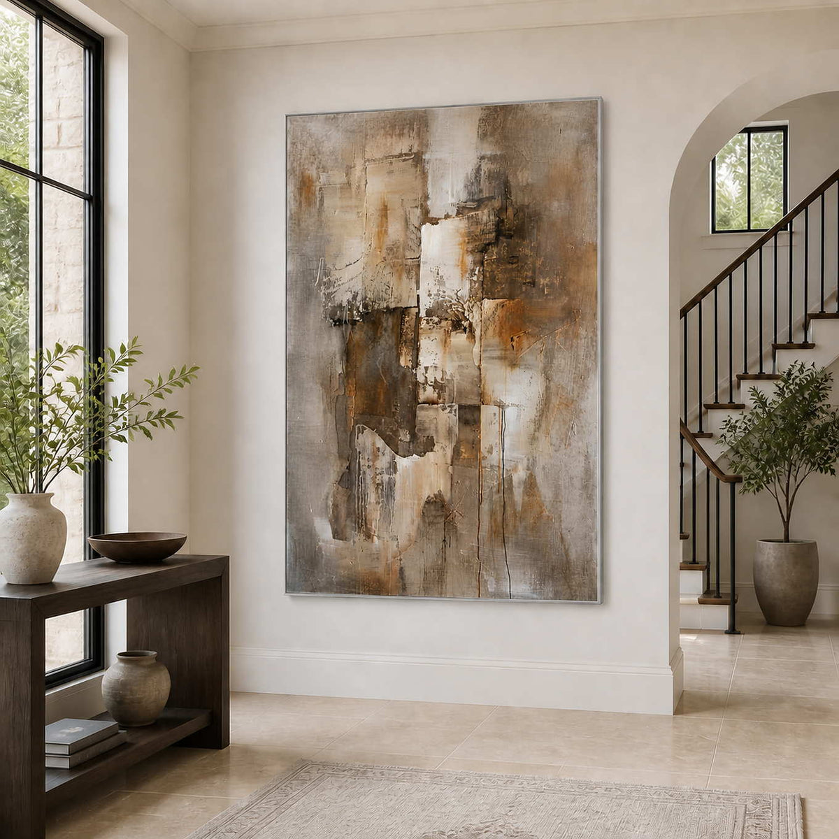 Silver-framed earthy abstract wall art beside an arched entryway staircase and dark wooden console.