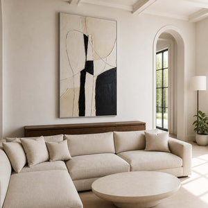 Silver framed monochrome abstract artwork above a sectional sofa beside an arched window.