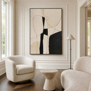 Black framed abstract painting between two cream reading chairs beside a slender floor lamp.