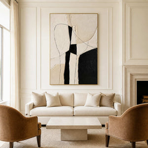 Gold framed ivory and black artwork above a cream sofa between warm brown armchairs.