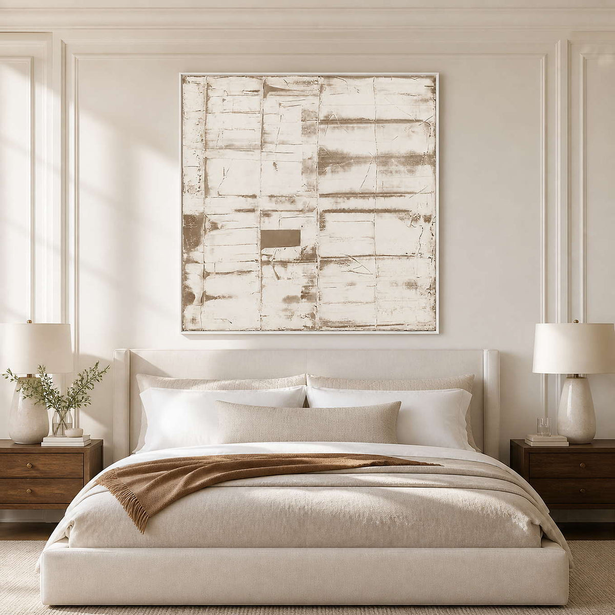 White-framed neutral abstract above an ivory bed with a brown throw and wooden nightstands.