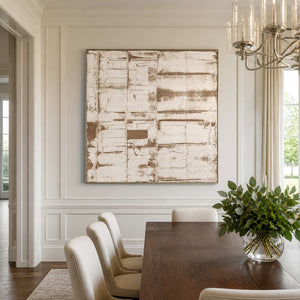 Silver-framed layered abstract beside a dark dining table, cream chairs and glass chandelier.