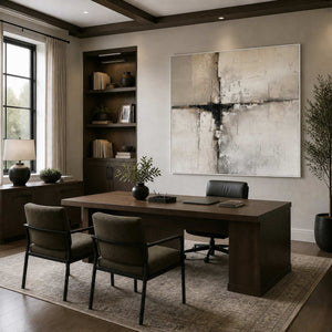 White framed neutral abstract artwork behind a wooden office desk beside dark built-in shelving.