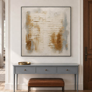 Ivory abstract painting with warm gold patches and horizontal raised lines in a black frame in an entryway.