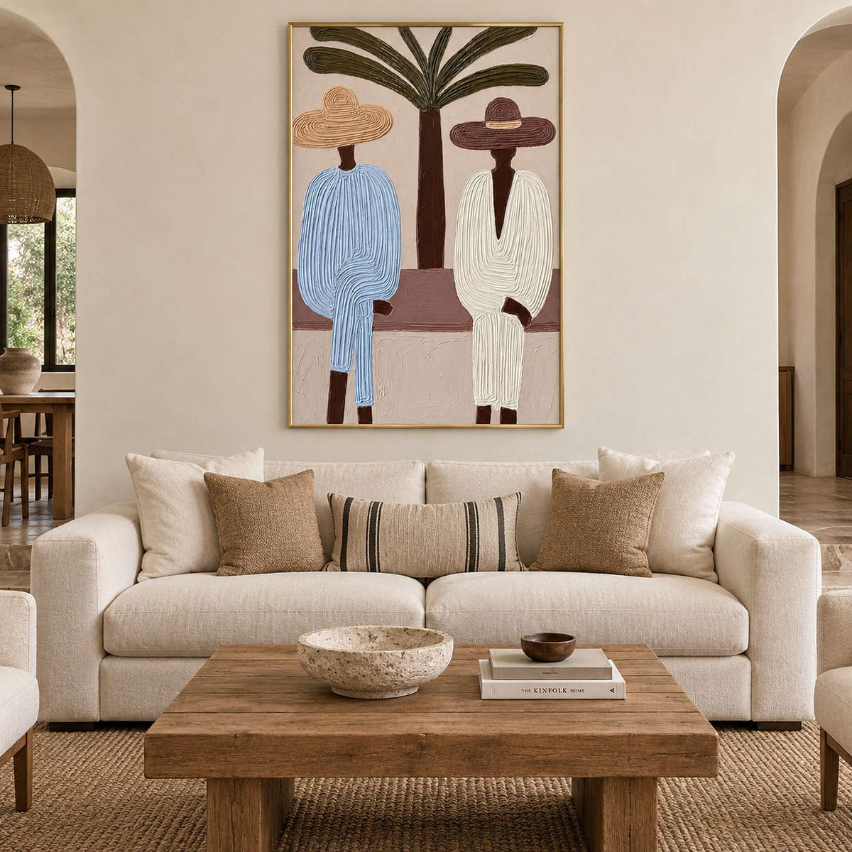 Palm and seated figures artwork above a cream sofa with striped and neutral cushions.