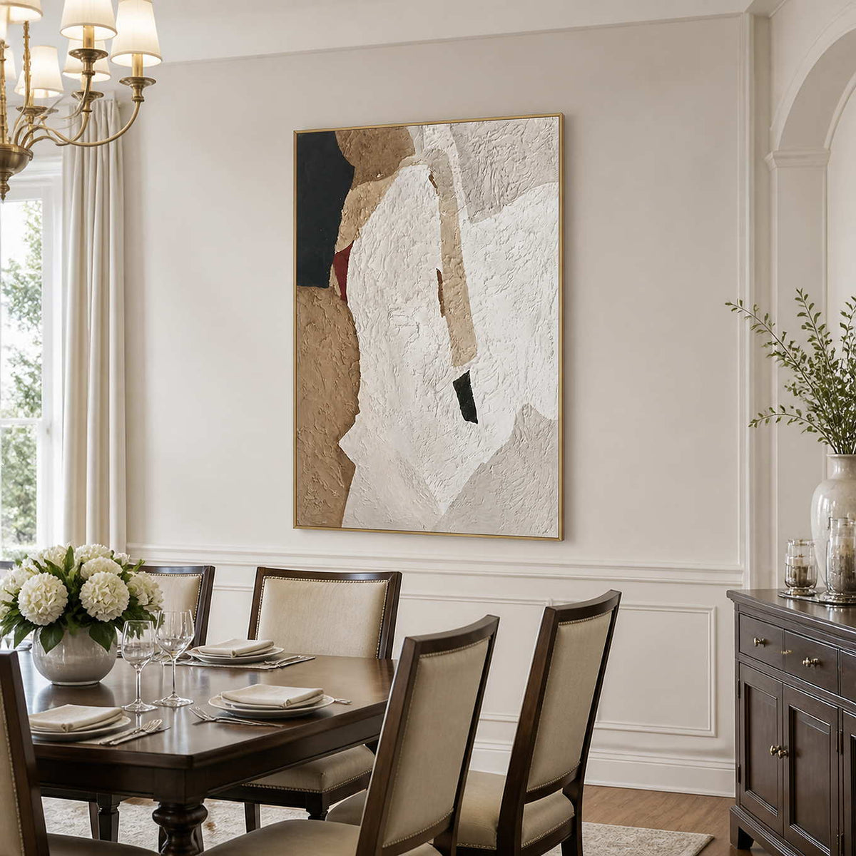 Gold framed earthy textured artwork above a dining table set with plates and white flowers.