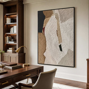 Black framed earthy textured artwork beside wooden bookshelves and a desk in a home office.