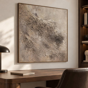 Irregular beige and taupe relief-like textures on a pale square ground in an artwork with a brown wood-look frame, displayed in a study with a desk.