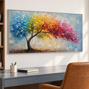 Rainbow tree painting with raised colorful leaves and a pale blue background in a silver frame in a home office.