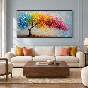 Rainbow tree painting with raised colorful leaves and a pale blue background in a black frame in a living room.