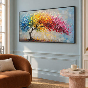 Rainbow tree painting with raised colorful leaves and a pale blue background in a black frame in a lounge.