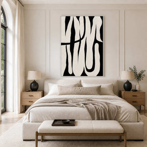 White framed black and white abstract artwork above a cream bed with wooden bedside tables.