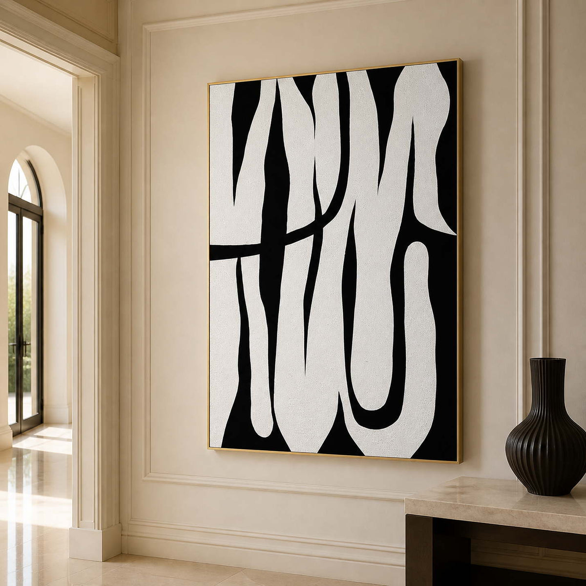 Gold framed monochrome curved artwork beside a pale console and black vase in a hallway.