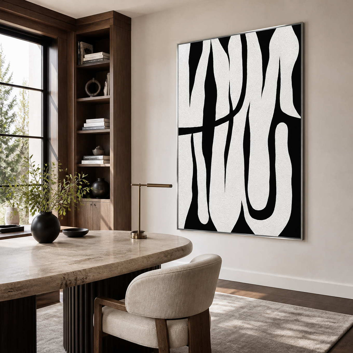 Silver framed curved abstract artwork beside wooden bookshelves above a pale stone office desk.