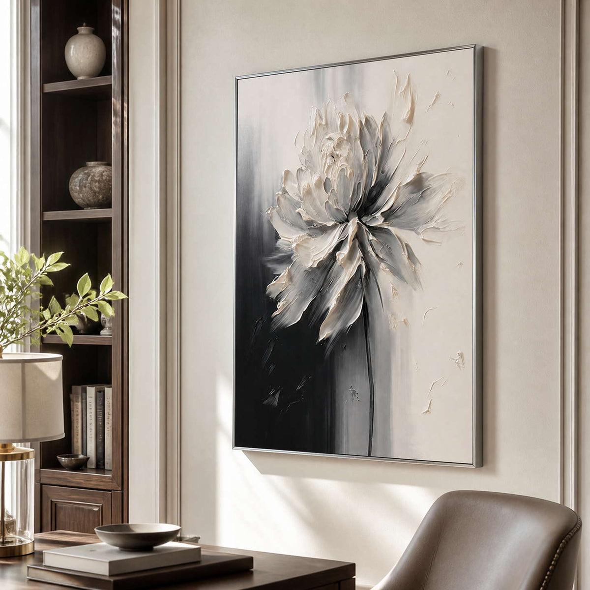 Silver framed ivory floral artwork beside a bookcase and leather study chair.