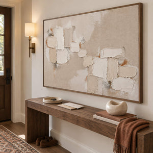 Textured abstract painting with raised ivory and taupe blocks in a brown wood frame in an entryway.