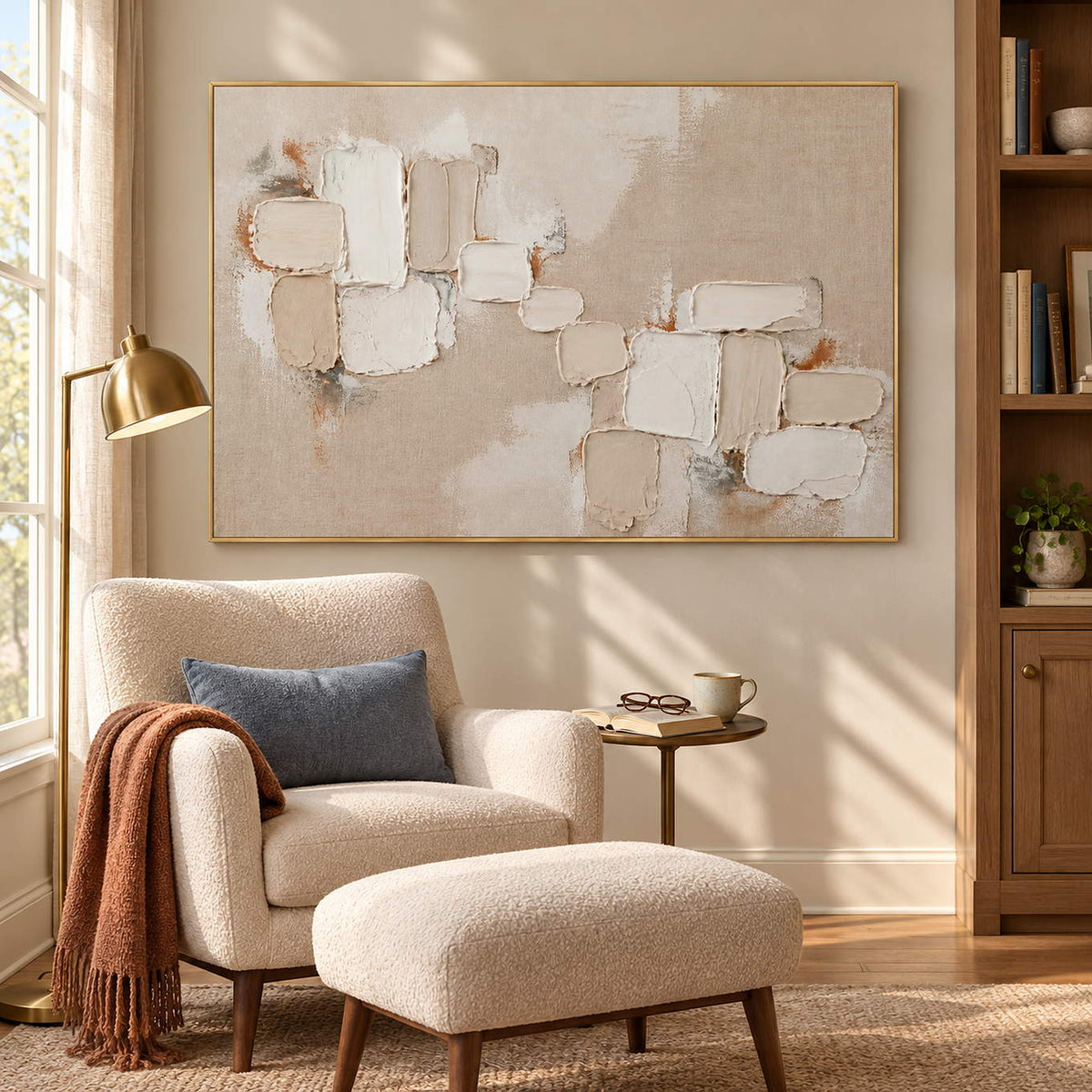 Textured abstract painting with raised ivory and taupe blocks in a gold frame in a sunlit seating area.